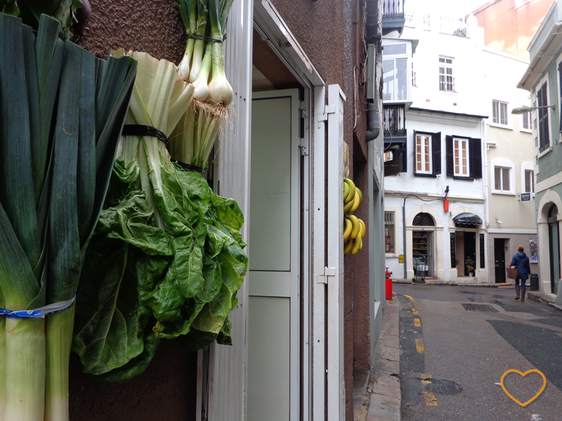 Uma loja tipo hortifruti com verduras e cachos de banana pendurados na fachada, como decoração.