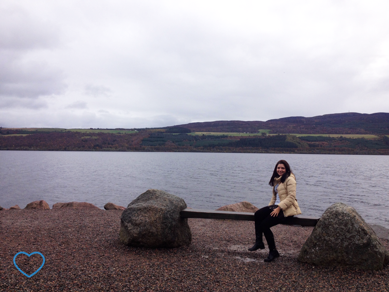 Foto do Lago Nesse e eu, sentada em um banco.