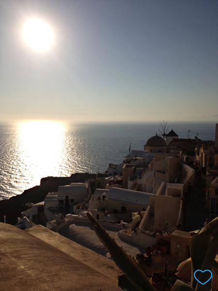 O famoso por do sol em Santorini. Vêem-se as típicas casas sob o sol poente e o mar com o reflexo do sol. E o próprio sol no céu.