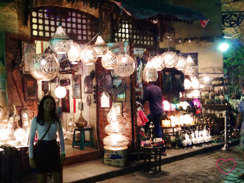 Eu em uma rua no centro histórico do Cairo, à noite. Estou diante de uma loja de luminárias, que estão acesas.