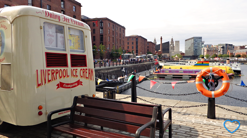 No enquadramento, está a parte traseira e uma komvi, onde está escrito "Liverpool ice cream". Ao fundo, a cidade de Liverpool.