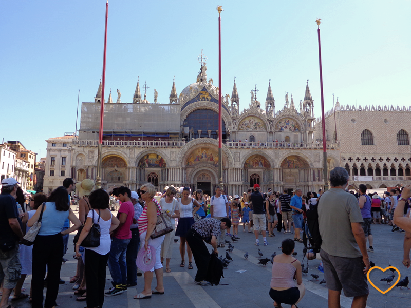 Foto na Piazza San Marco. Muitos turistas e pombas. Dia ensolarado e quente.