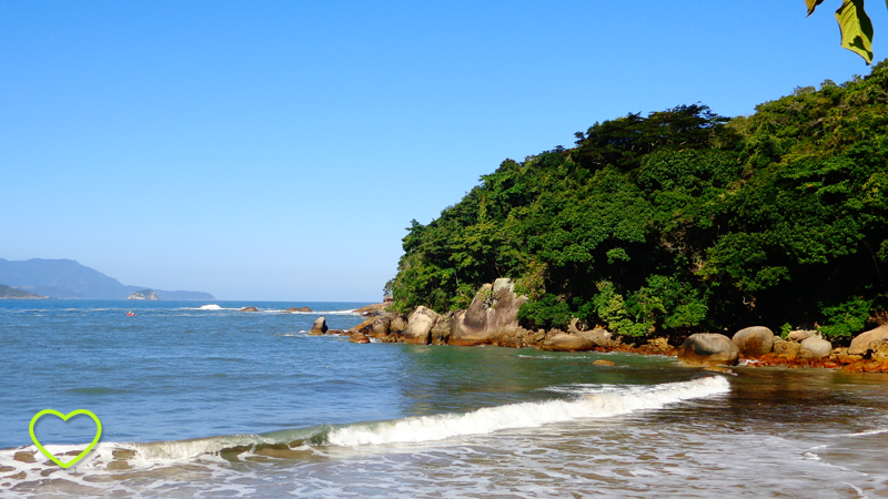 O mar bem azul, a espuma bem branca, um monte coberto por uma vegetação verde e vibrante.