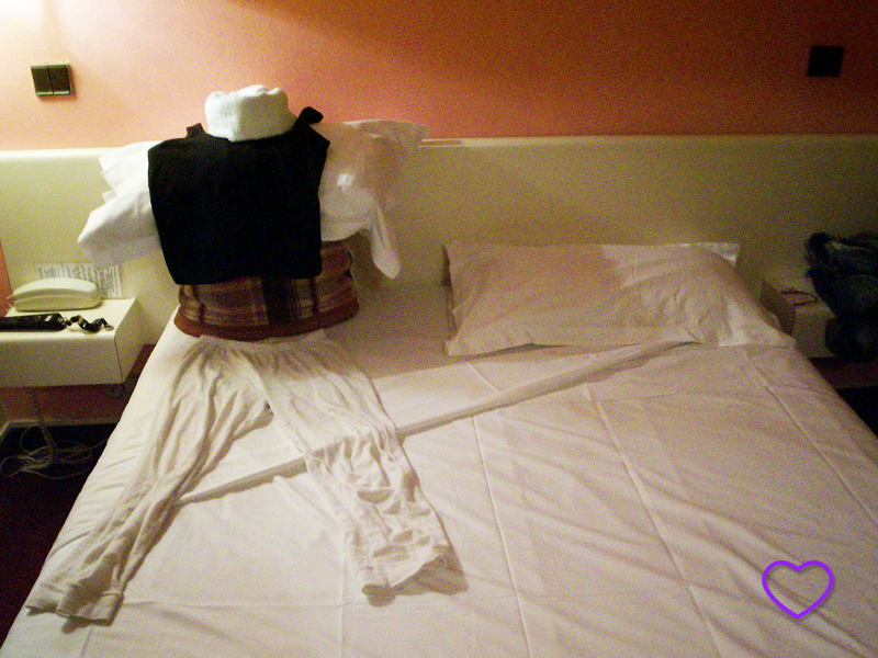 Foto do tal boneco em cima da cama, feito com lençol, cobertor e pijama.