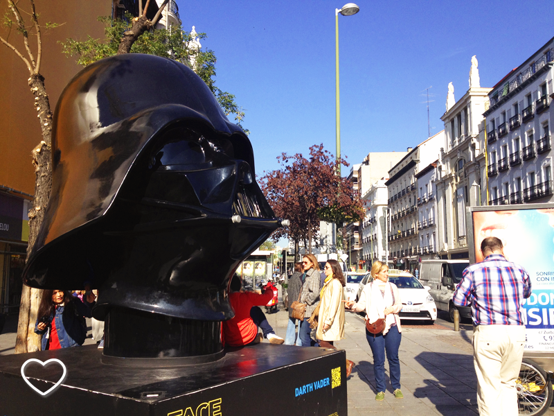 O capacete do Darth Vader de frente. Ao fundo, edifícios.