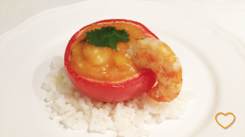 Bobó de camarão dentro de um tomate assado e aberto. Um camarão na borda e uma folha de salsinha no bobó.